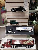 Four collectible model vehicles including two vintage cars and two semi trucks with trailers shown on display with a tag.