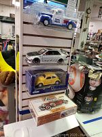 Photo showing the five model vehicles displayed on a wall mount including a sealed Lindberg 1932 Lincoln Phaeton model kit, a yellow Sunnyside Volkswagen Beetle in box, a white Lexus IS300 model, and a blue and white Dinty Moore pickup truck model in display case.