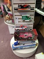 Five collectible model cars and trucks shown stacked including boxed and unboxed models on a white display pedestal.