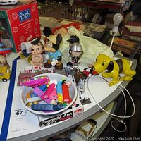 Photo of collection of toys on table including Pez dispensers, raggedy Ann & Andy radio with box, pull toy dog, Mickey Mouse figure, bobbleheads, and vintage firetruck.