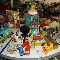 Wide view of the collection showing multiple vintage toys on a white table, including Pooh Christmas go round in original box, Fisher Price turtle, Mickey Mouse figure, red and blue toy cars, a yellow dog toy, and wooden blocks.