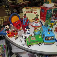 Full view of table with vintage and newer toys including Lincoln Logs box, Mickey Mouse toys, Scooby Doo van, and other toys arranged for visual inventory.