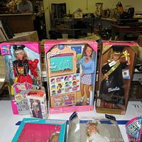 Three Barbie dolls and a keychain in original packaging displayed on table.