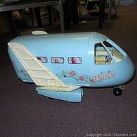 Side view of the light blue Barbie airplane toy showing floral decals, windows, cockpit with dolls, and attached wing and engine.