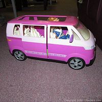 Side view of pink and white Barbie Volkswagen-style van with sliding side door open and Barbie doll in blue polka dot dress seated inside