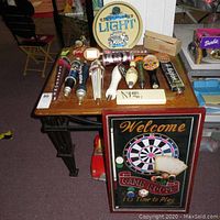 Photo of beer tap handles, round Miller Lite beer sign on a wooden table, and framed game room sign leaning against the table