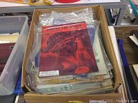Box of assorted vintage sheet music, focusing on 'Around The World' title with red cover and hot air balloon graphic.