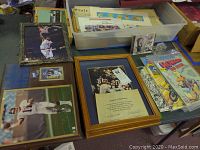 Overview of lot showing framed sports photograph, comic books, newspapers, and other items on table.