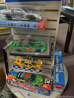 Wide photo showing four Nascar cars in display cases and boxes, and two Getty chopper trucks in original blue boxes on a shelf