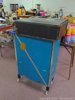 Blue child's magician case on wheels with black top and gold and silver diagonal stripes