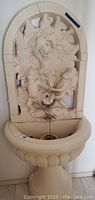 Full view of the cream-colored angel birdbath statue with three cherubs in a garden relief and a basin below