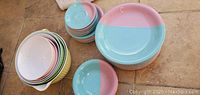 Collection of pink and blue dishes including large plates, bowls, and smaller plates stacked on a tile floor with yellow nesting mixing bowls.