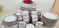 Full set of holly print dishes including stacked plates, cups, and bowls showing the overall quantity and design.