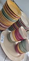 Stacked small plates of varied colors including yellow, red, green, and white with stacked bowls nearby.