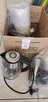 Chefman glass tea kettle in cardboard box alongside glassware and kitchen appliances