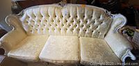 Front view of the cream-colored sofa with tufted back and floral upholstery pattern showing upholstery condition and wood frame details.