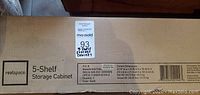 Label on the box showing brand Realspace, product name 5-Shelf Storage Cabinet, color black, quantity 1, model details and pallet sticker with lot number.