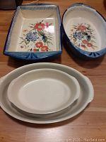Four ceramic bakeware pieces with floral designs: two with floral interiors and blue rims, two plain white oval dishes