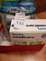 Photo showing Crest Glide dental floss 6 pack and Philips Sonicare branded box in bin