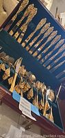 Set of F.B. Rogers gold toned knives, forks, and spoons with intricate embossed floral design housed in a blue velvet lined wooden box.