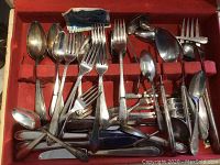 Overhead view of open wooden box filled with mixed flatware piled in velvet compartments