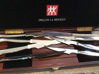 Close-up photo of one wooden box of Zwilling J.A. Henckels knives showing polished stainless steel blades and black handles.