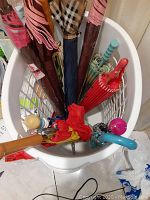Photo of umbrella collection standing inside a laundry basket showing various handles and umbrella tops with different colors and patterns.