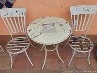 Front view of two wrought iron chairs and round table showing paint chipping and rusting