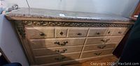 Front view of the dresser showing multiple drawers with metal handles and keyhole accents, featuring a marbled laminate top and carved wood accents.