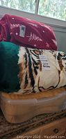 Two plush blankets rolled and stacked on a container, one red with white tree and snowflake pattern and one tiger print with green edging.