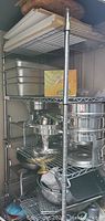 Chrome-plated wire shelving unit loaded with chafing dishes, pans and fuel canisters
