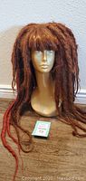 Front view of the Kanekalon dreadlock wig on beige mannequin head, showing thick reddish dreadlocks with bangs.