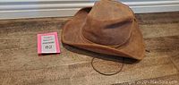Brown genuine leather cowboy hat on floor with MaxSold lot tag.