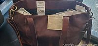 Brown genuine leather handbag with top handles and detachable shoulder strap, showing tags and auction label.