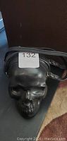 Front view of skull-shaped black crossbody bag showing the zipper closure along the top and strap attached to sides.