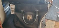 Front angled view of black leather handbag showing overall shape and handles