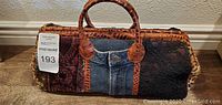 Front view of handbag showing patchwork pattern with denim center pocket and faux crocodile leather handles.