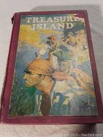 Front cover of a 1924 treasure island book with colorful pirate illustration and worn maroon binding.