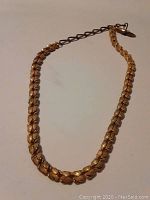 Full view of vintage gold-tone textured leaf-shaped linked necklace with attached darker metal chain.