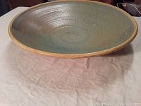 Large round ceramic bowl with spiral design and matte glaze shown from front angle on tablecloth.