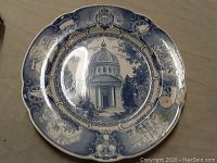 Blue and white Wedgwood ceramic decorative plate with a scalloped edge and central image of The Chapel US Naval Academy, featuring colonial motifs around rim. Flaw indicated by arrow sticker on plate surface.