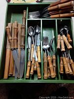Green storage tray containing bamboo handle flatware including forks, spoons, teaspoons, and steak knives.