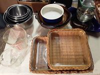 Photo showing a collection of baking and kitchenware items including stainless steel bowls, Pyrex measuring cups, ceramic casserole, glass bowls, and woven wicker trays