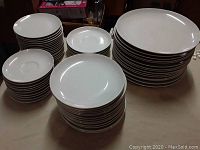 Photo showing multiple stacks of plain white ceramic plates in various sizes, totalling 61 pieces.
