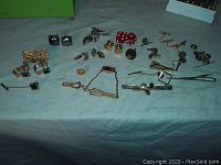 Wide view of the entire lot showing cuff links, tie clips, pins and other small men's jewelry items spread out on a surface.