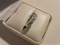 Side angle view of a sterling silver ring with five rectangular clear stones on top, displayed in a white jewelry box.