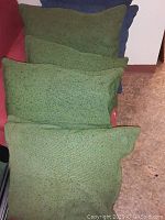 Green and blue goose down throw pillows arranged side by side and stacked on a reddish sofa and nearby floor area.