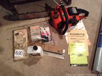 Photo of Echo orange chain saw with 16-inch blade showing visible wear on blade and chain. Several accessories and instruction manuals laid out on concrete surface nearby.