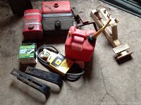 Overview of three fuel tanks, red gas can, belts, hitch parts, safety grit tape, and seat spring attachment on concrete floor