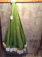 Closed large vinyl patio umbrella in green with white fringe.